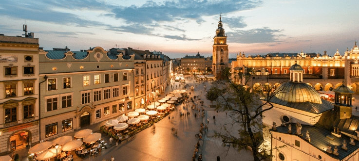 Elevated view of Krakow's Main Square at dusk, with the iconic Town Hall Tower and Cloth Hall illuminated, as locals and tourists enjoy the vibrant market area, epitomizing Poland's welcoming stance as a cryptocurrency-friendly nation
