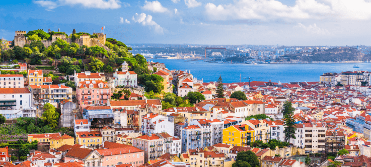Panoramic view of Lisbon, Portugal, showcasing the historic São Jorge Castle overlooking a colorful tapestry of buildings and rooftops with the Tagus River in the background, illustrating the city's allure as a crypto tax haven